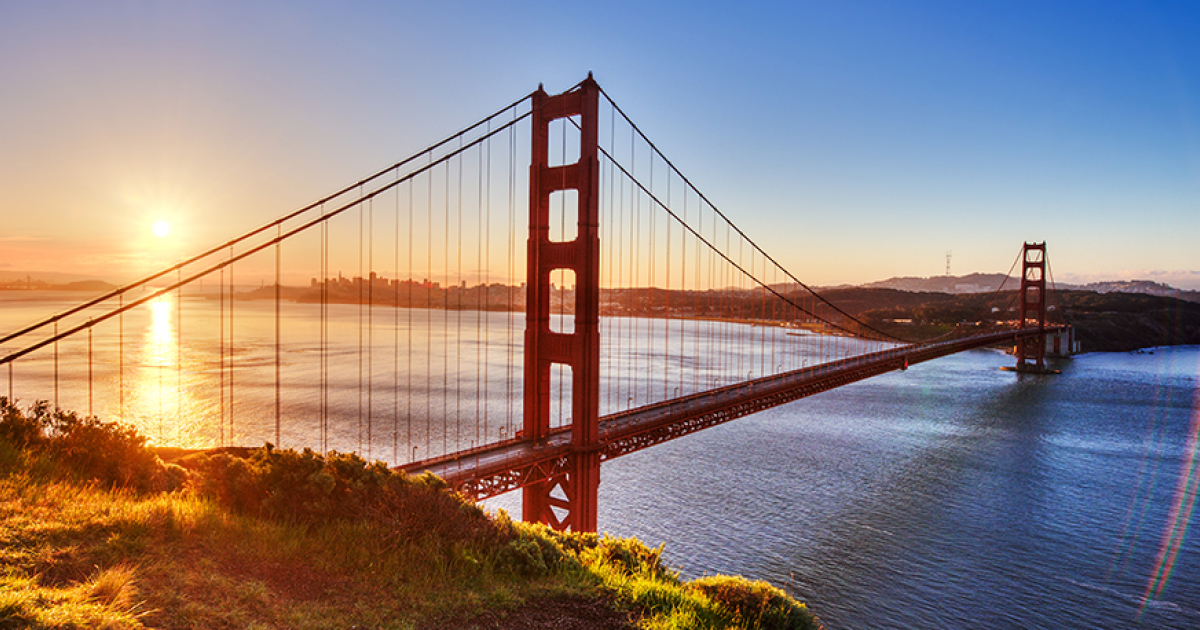 The Golden Gate Bridge at sunrise, viewed from the Marin Headlands, with the San Francisco skyline visible in the distance.